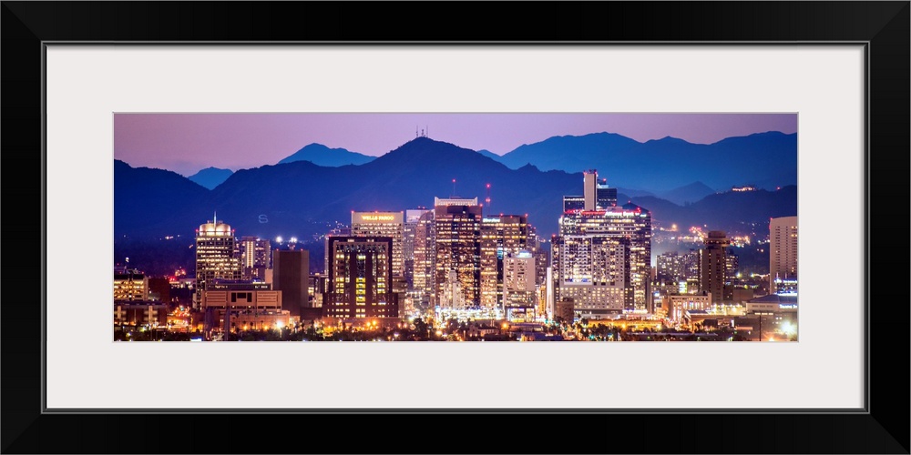 Panoramic photograph of a colorful sunset over the Phoenix, Arizona skyline with silhouetted mountains in the background.