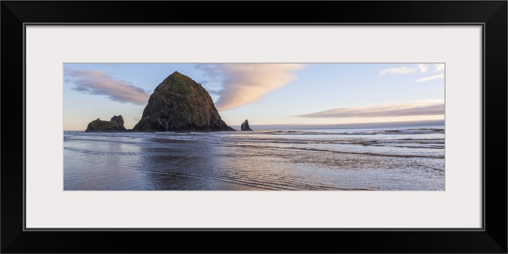 Panoramic photograph of Haystack Rock with a pink and purple sunset and reflections on the water.