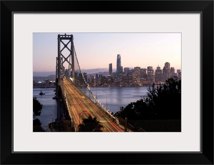 Photograph of the Bay Bridge with a pink and purple sunset and the San Francisco skyline lit up in the background.