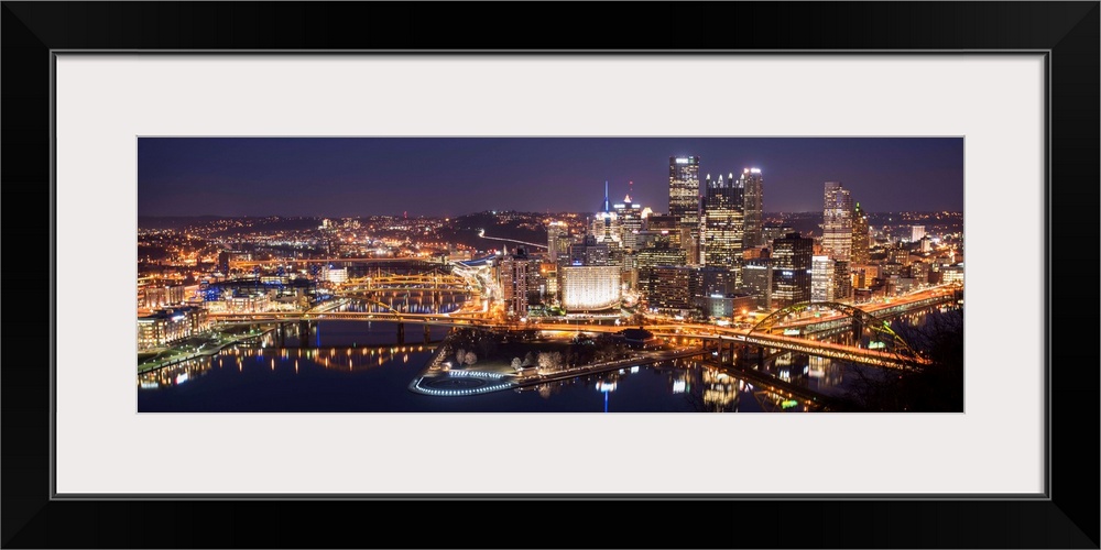 Panoramic photo of the city of Pittsburgh illuminated at night, with Point State Park in the foreground.
