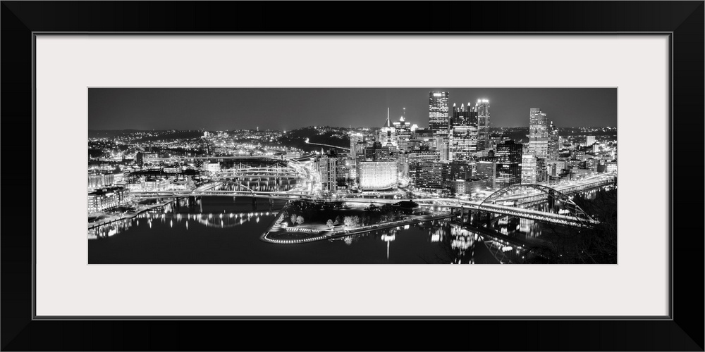 Panoramic photo of the city of Pittsburgh illuminated at night, with Point State Park in the foreground.