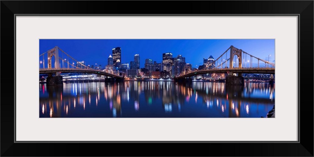 Panoramic view of the Pittsburgh city skyline in the evening reflected in the water, with two of the Three Sisters bridges...