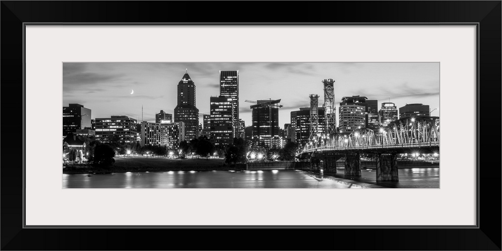 Panoramic photograph of the Portland, Oregon skyline lit up with lights at the beginning of sunset with a small crescent m...