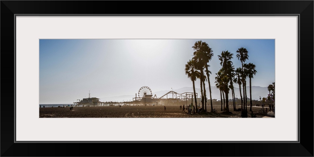 Panoramic photograph of the Santa Monica Pier in Los Angeles, California, with palm trees in the foreground and a purple h...