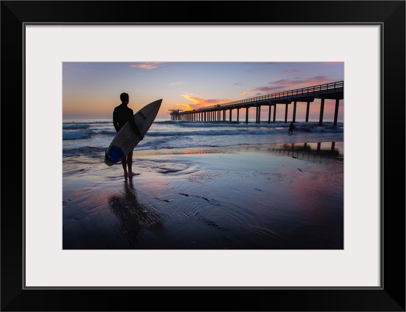 Silhouetted photograph of a man holding a surf board on the shore of Ocean Beach in San Diego, California, with the Ocean ...