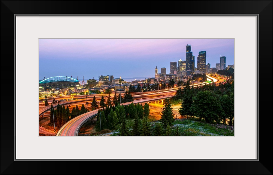 Panoramic photograph of the Seattle skyline at night with light trails from the car lights on the highway.