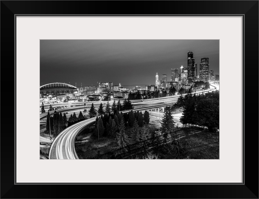 Panoramic photograph of the Seattle skyline at night with light trails from the car lights on the highway.