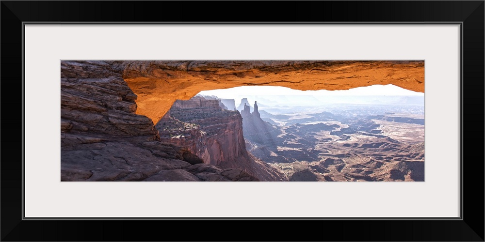 The underside of the Mesa Arch glowing bright orange with sunlight, with Buck Canyon in the distance, Canyonlands National...