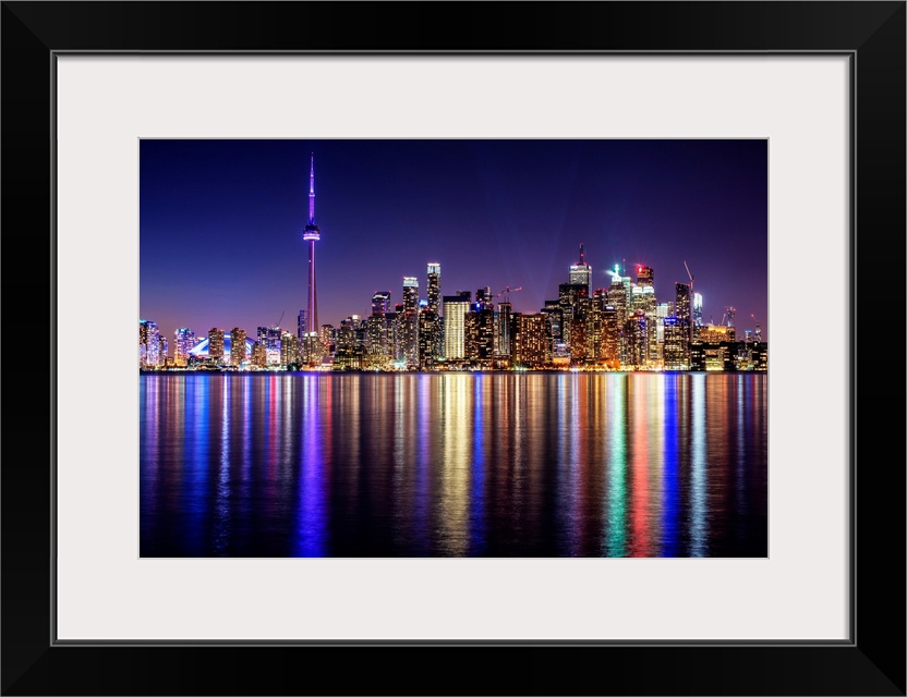 Photo of the Toronto city skyline with lights reflected in the water at night.