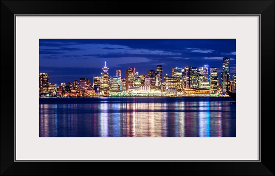 Photograph of the Vancouver, British Columbia skyline lit up on a dark blue night and reflecting bands of colorful light o...