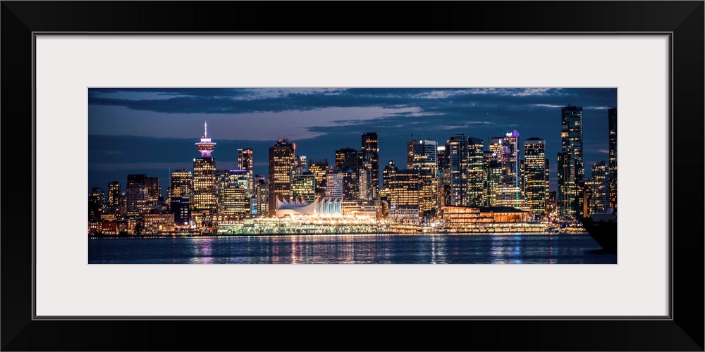 Panoramic photograph of the Vancouver, British Columbia skyline lit up on a dark blue night and reflecting bands of colorf...