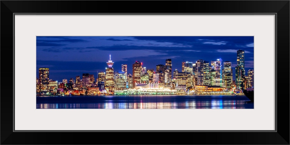 Panoramic photograph of the Vancouver, British Columbia skyline lit up on a dark purple night and reflecting bands of colo...