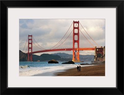 A couple strolling on Baker Beach near the Golden Gate Bridge at dawn