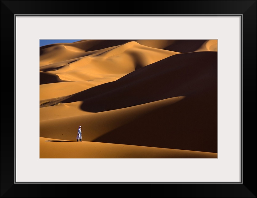 Berber man walking among the orange sand dunes of the Erg Chebbi sand sea, Sahara Desert near Merzouga, Morocco, North Afr...