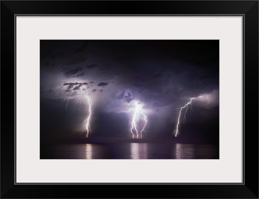 Time-lapse photo of three bolts of lightning striking the ocean from storm clouds at night, illuminating the dark sea.