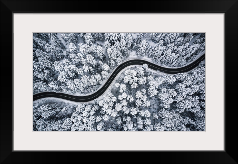 Curvy windy road in snow covered forest, top down aerial view.