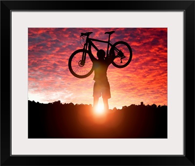 Silhouette Of a mountain biker holding up bike against a sunset sky