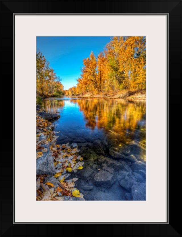 A clear blue sky fall day with colorful trees reflecting along Mission Creek British Columbia, Canada.