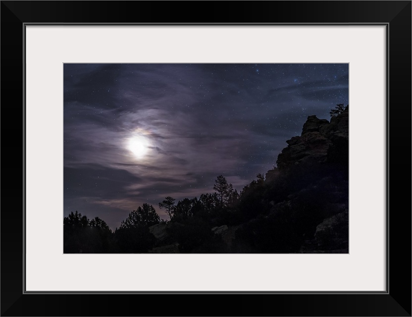 A bright moon rises through clouds over a hill in Oklahoma, USA.