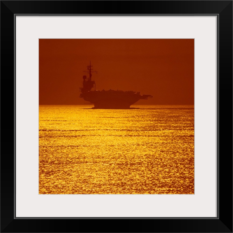 Square photograph on a large wall hanging of a silhouetted aircraft carrier on vivid golden waters and a red sky, as the s...