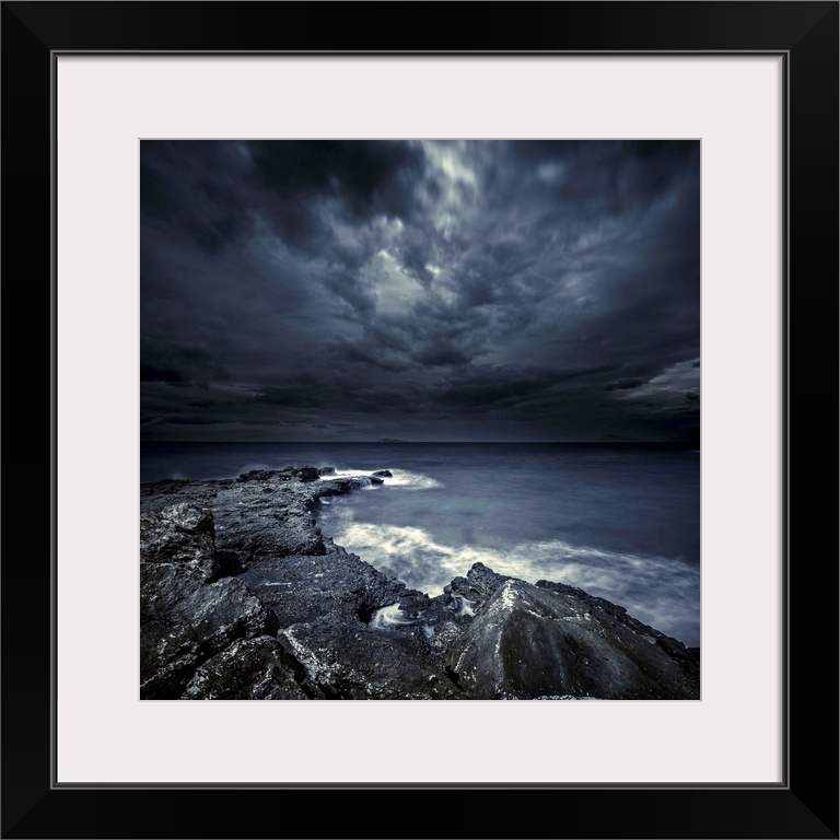 Black rocks protruding through rough seas with stormy clouds, Crete, Greece.