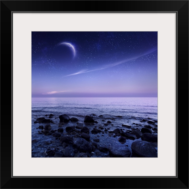 Moon rising over rocky seaside against starry sky.