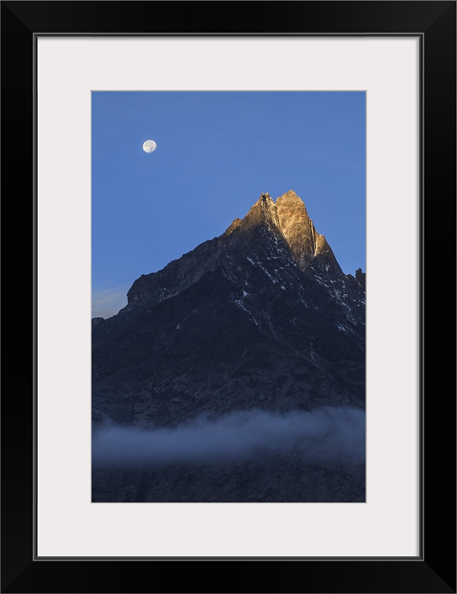 Moonset and alpenglow over a snow peak in the Himalayas as seen from Sagarmatha National Park of Nepal.