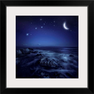Rising moon over ocean and boulders against starry sky