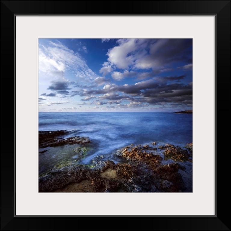 Tranquil lake and rocky shore against cloudy sky, Hersonissos, Crete, Greece.