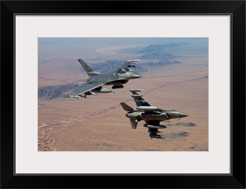 Two F-16's from the 56th Fighter Wing at Luke Air Force Base, Arizona, manuever on a training mission over the Arizona des...