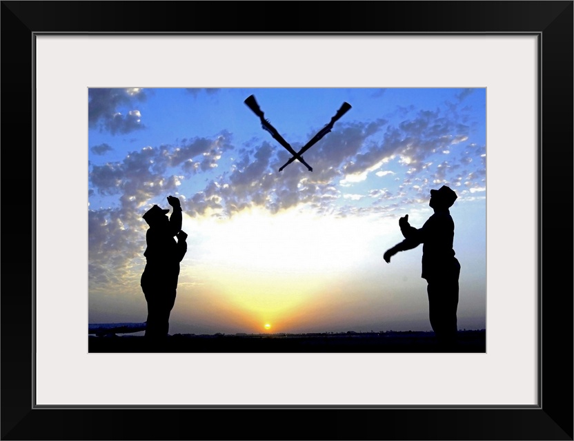 Photograph of two silhouetted soldiers tossing rifles with sunset in distance under a cloudy sky.