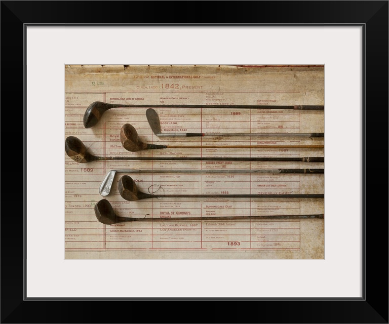 Antique golf clubs are lined up and lay over a vintage poster of major golf tournaments.