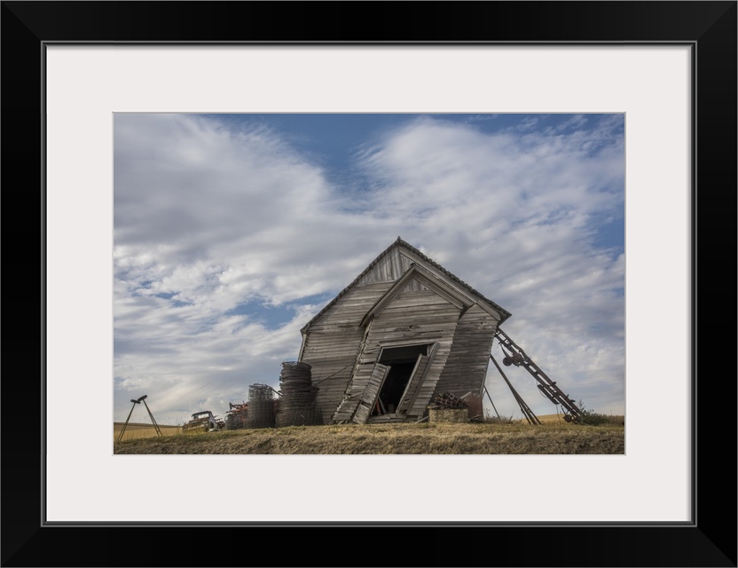 Abandoned schoolhouse building leaning heavily to the side, against a backdrop of clouds, Palouse, Washington.