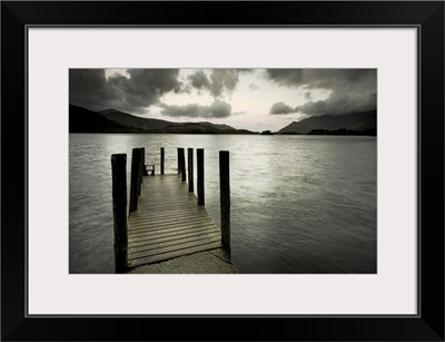 A small wooden jetty looking out over a lake with stormy clouds over a dark headland