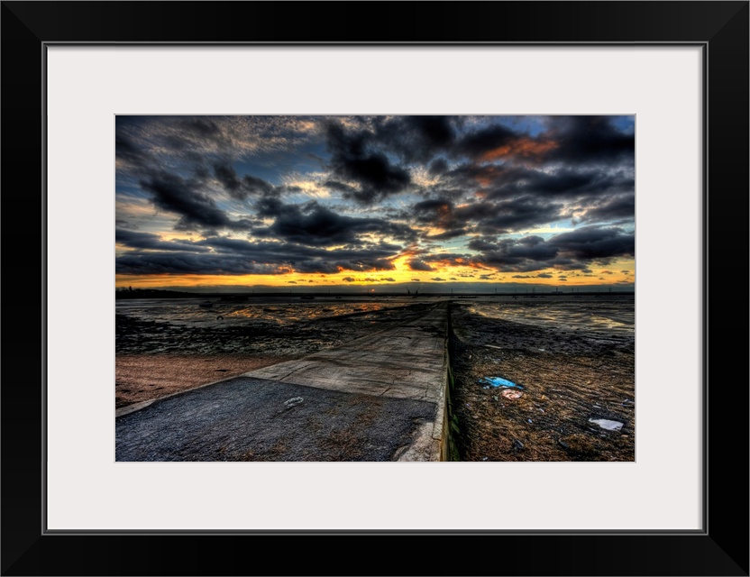 Cloudy evening sunset over an estuary with dramatic stormy clouds looking out over a causeway with cranes on the horizon