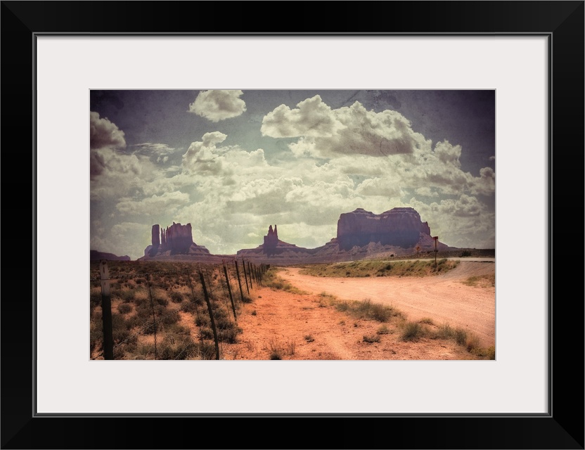 Large monolithic rocks in the background looking through Monument Valley in the United States, with desertic road and clou...