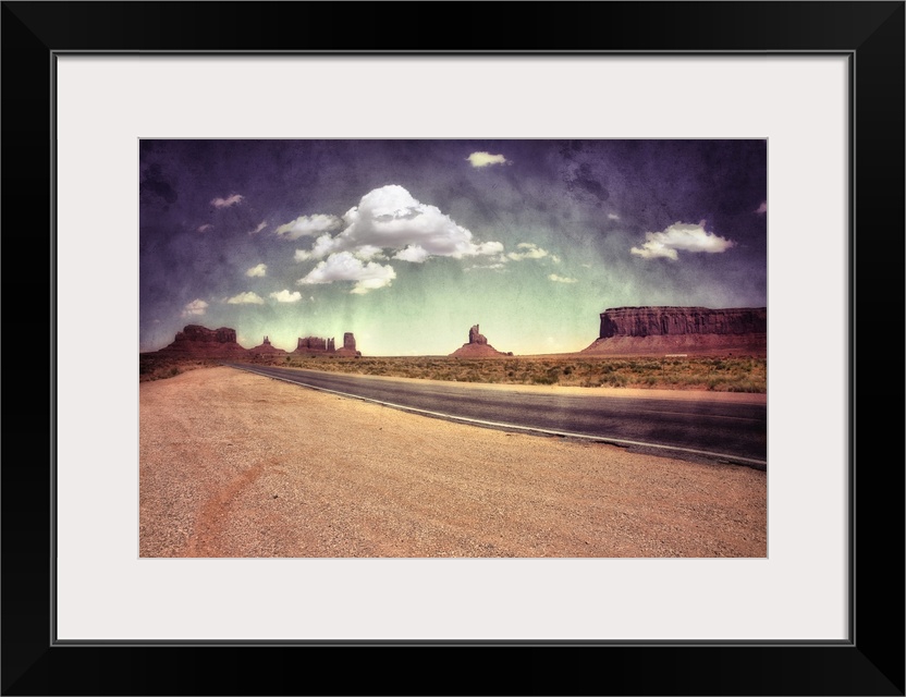 Large monolithic rocks in the background looking through Monument Valley in the United States, with desertic road and clou...