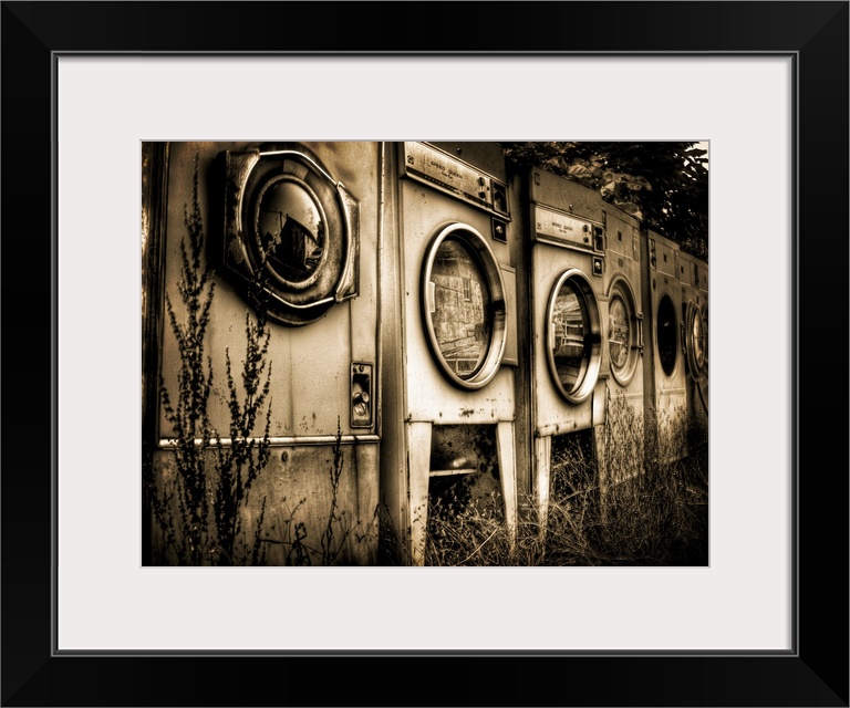 Redundant washing machines in a row left outside with grass growing