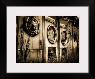 Redundant washing machines in a row left outside with grass growing