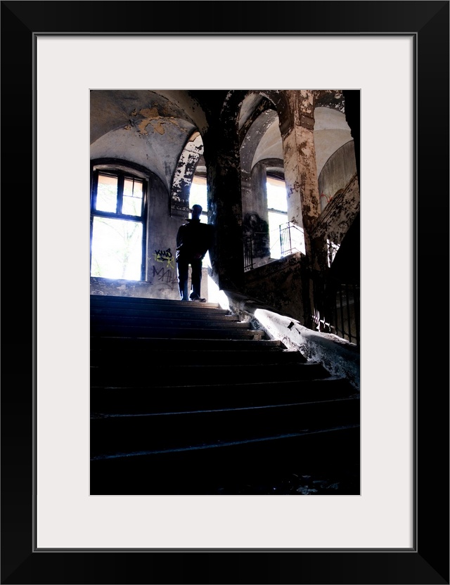 Silhouette of a man standing on some old stairs in a large building