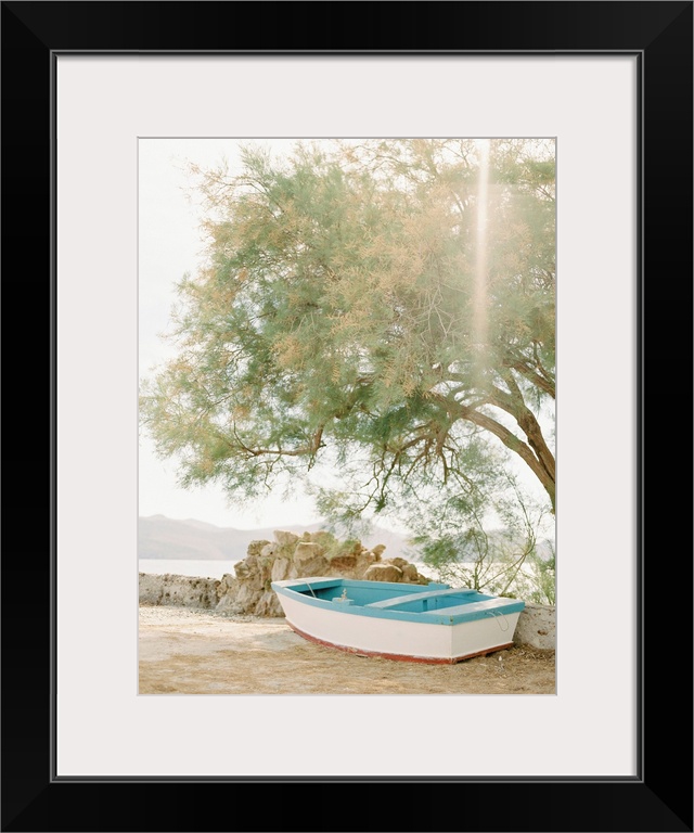 Photograph of a small wooden boat underneath a tree next to the water, Milos, Greece.