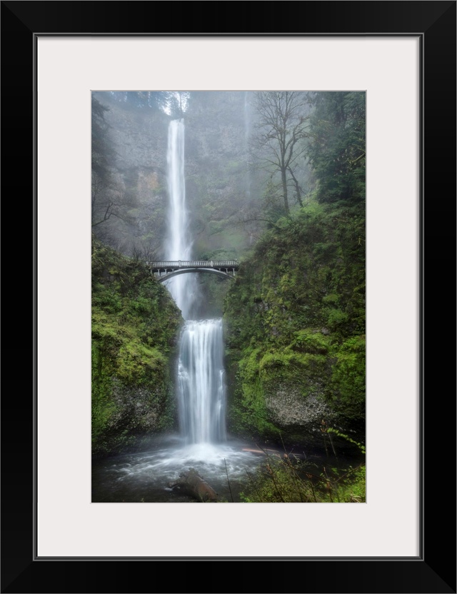 Photograph of a serene waterfall among vibrant greenery vegetation in the mist.