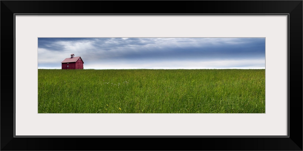 Panoramic photograph of a rural landscape with a wide open green field, red barn, and a blue cloudy sky.