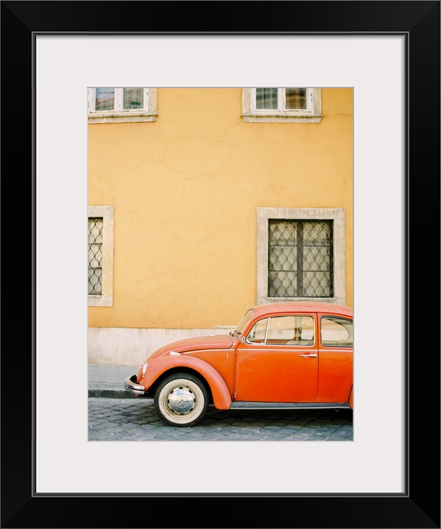 Photograph of an orange Volkswagen Beetle car parked in front of a yellow wall, Budapest, Hungary.