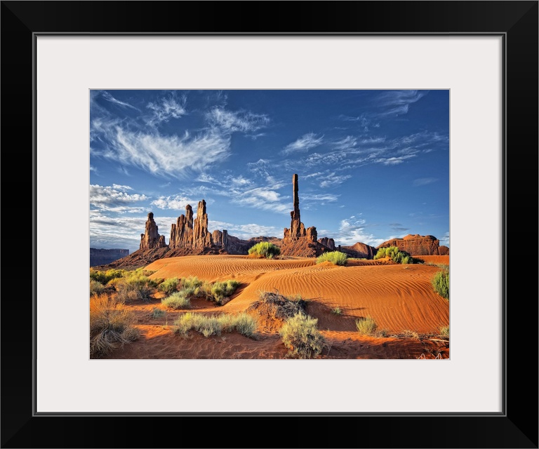 This bright photo features a contrasting desert landscape with sandy hills and large rock formations against a bright blue...