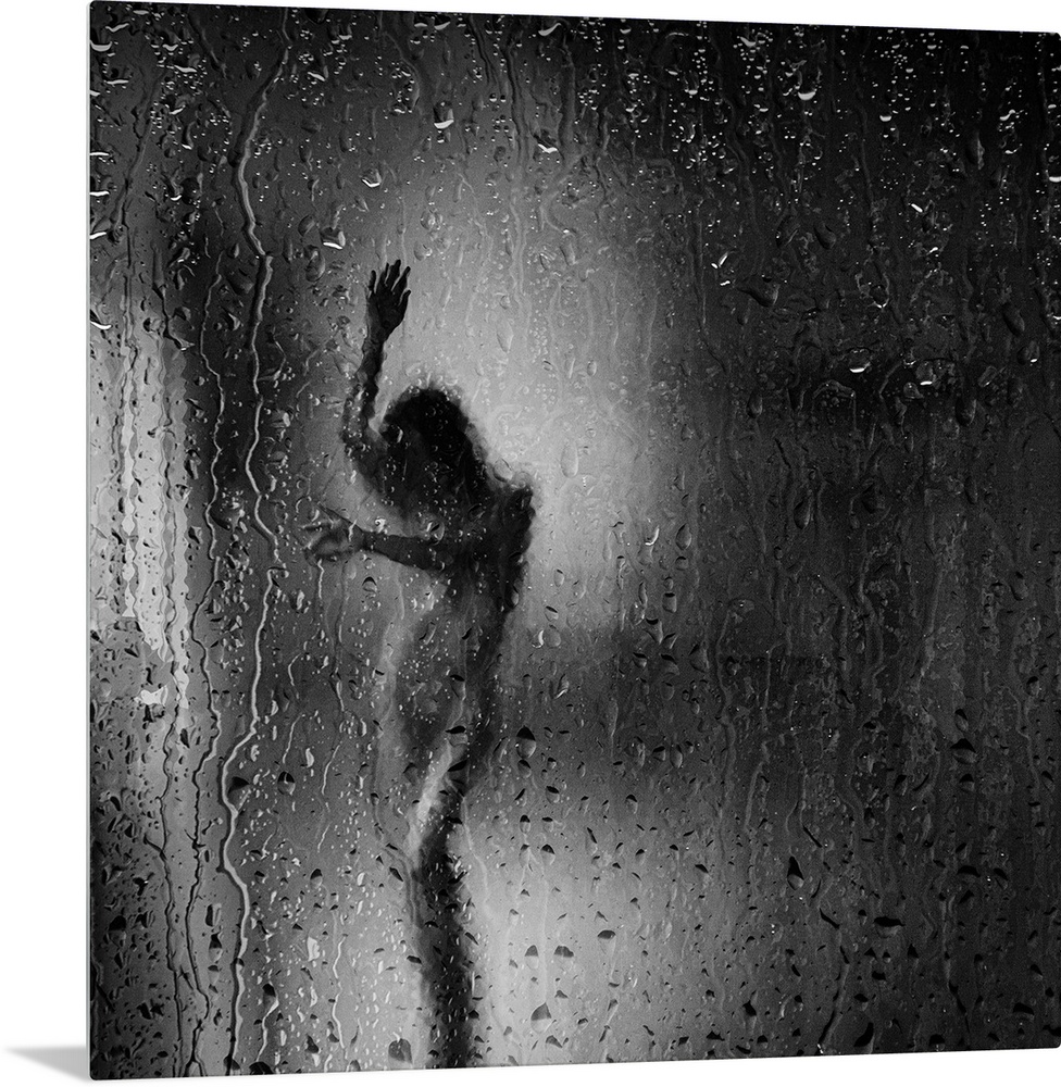 Square black and white fine art photograph of a nude woman through a rainy window glass.