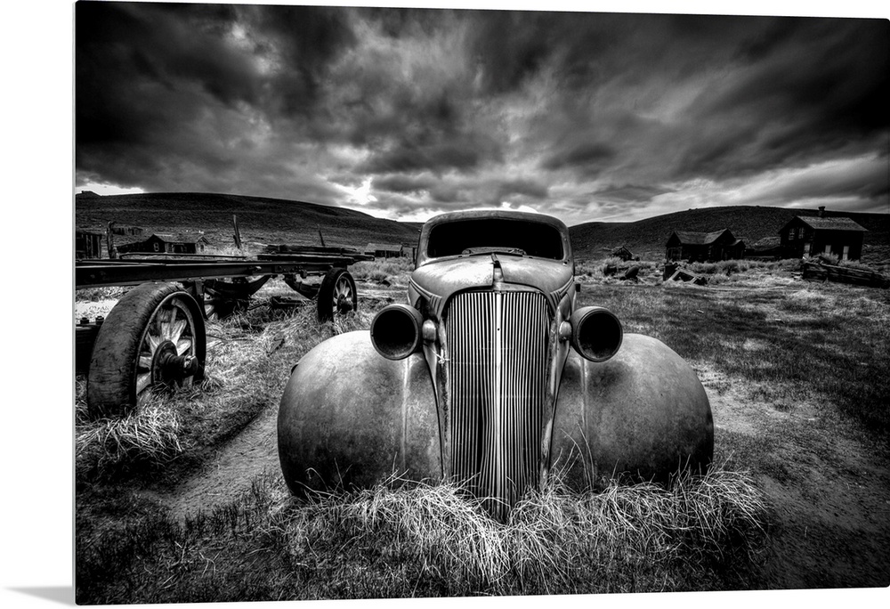 A black and white photograph of derelict vintage car sitting in a desert landscape.