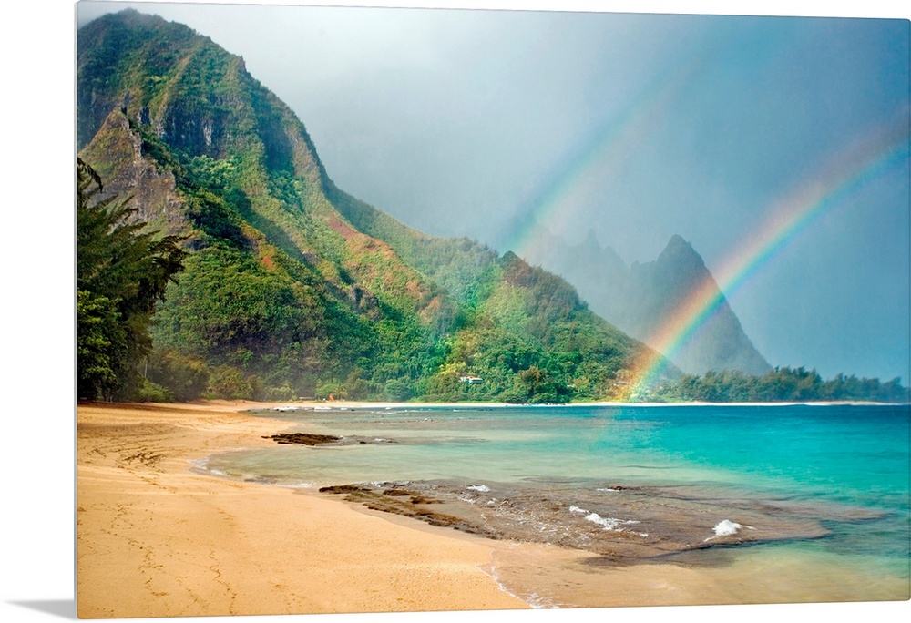 A landscape photograph with double rainbows on a tropical beach with mountains in the background.