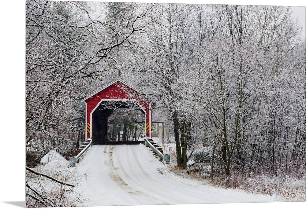 Snow covered trees surround a road that leads up to a covered bridge.