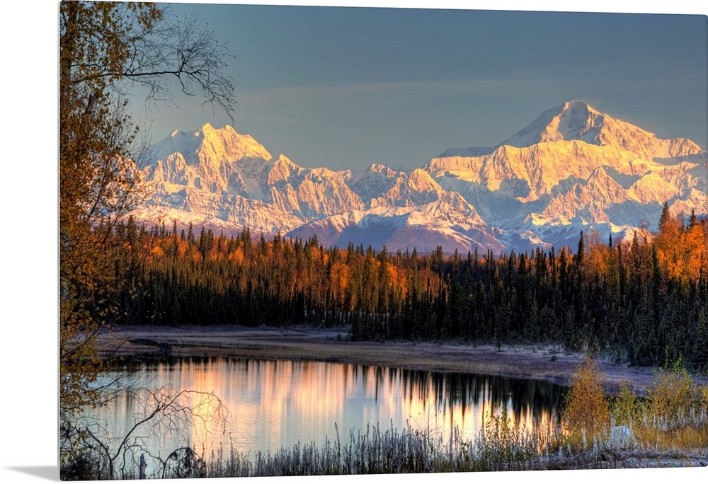Serene landscape at dawn of two snow-covered mountains near a pine forest at the edge of a small pond in Alaska.